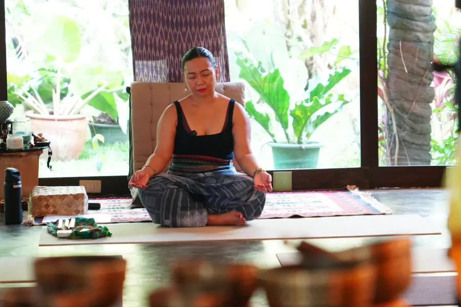 Rina meditating cross-legged in a garden pavilion